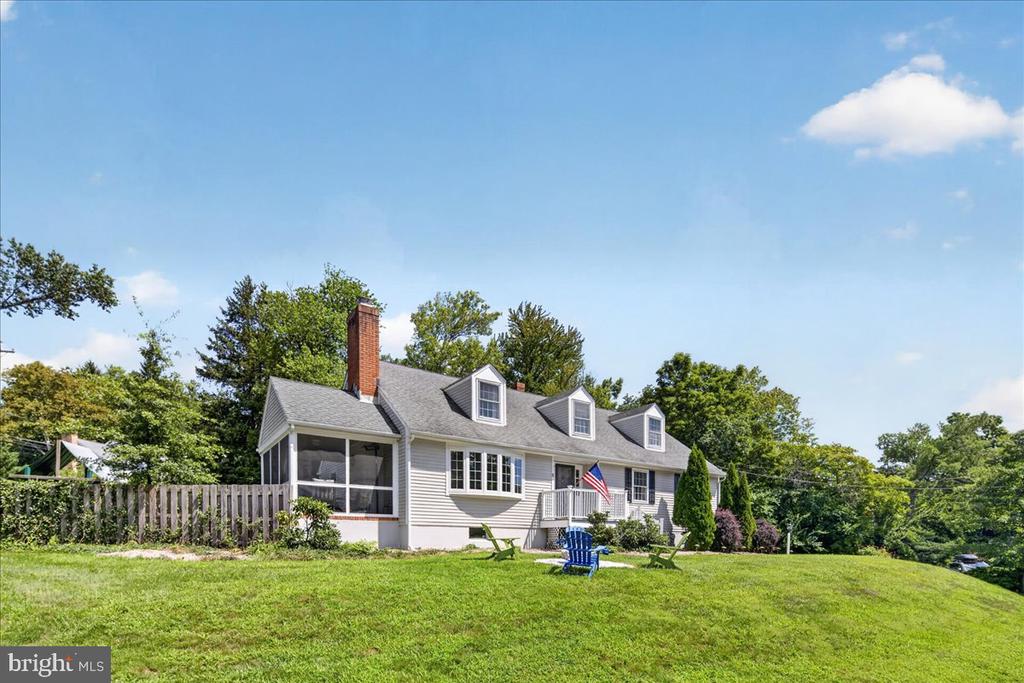 Gray-sided home with three dormers, a screened porch, and a broad green lawn.