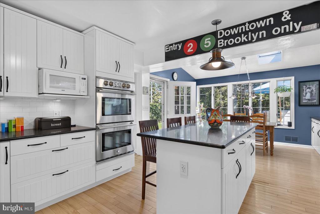 Kitchen with white cabinets, double ovens, and a large island beside a sunny dining area.