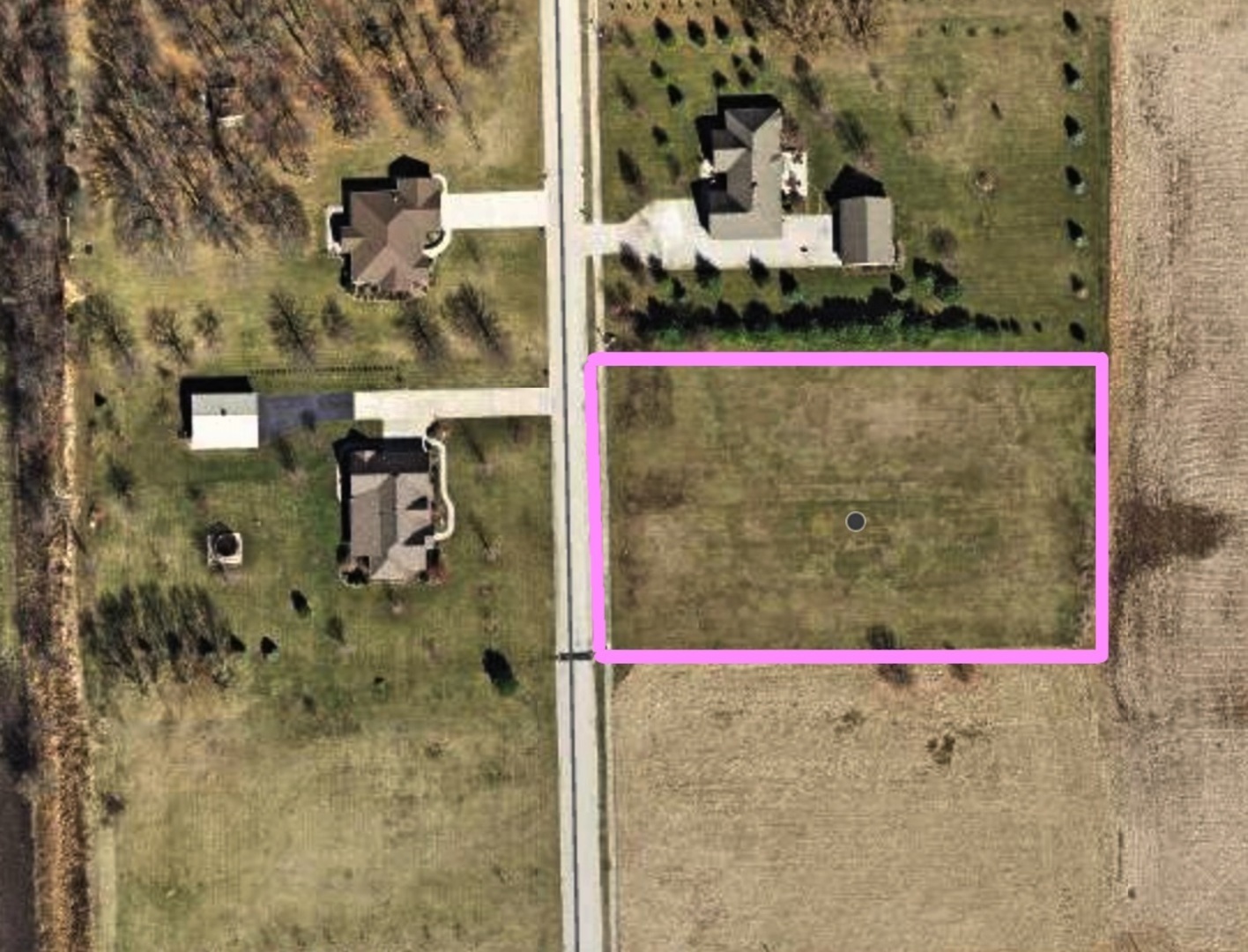 Vacant grassy parcel outlined in pink beside a road and neighboring homes.