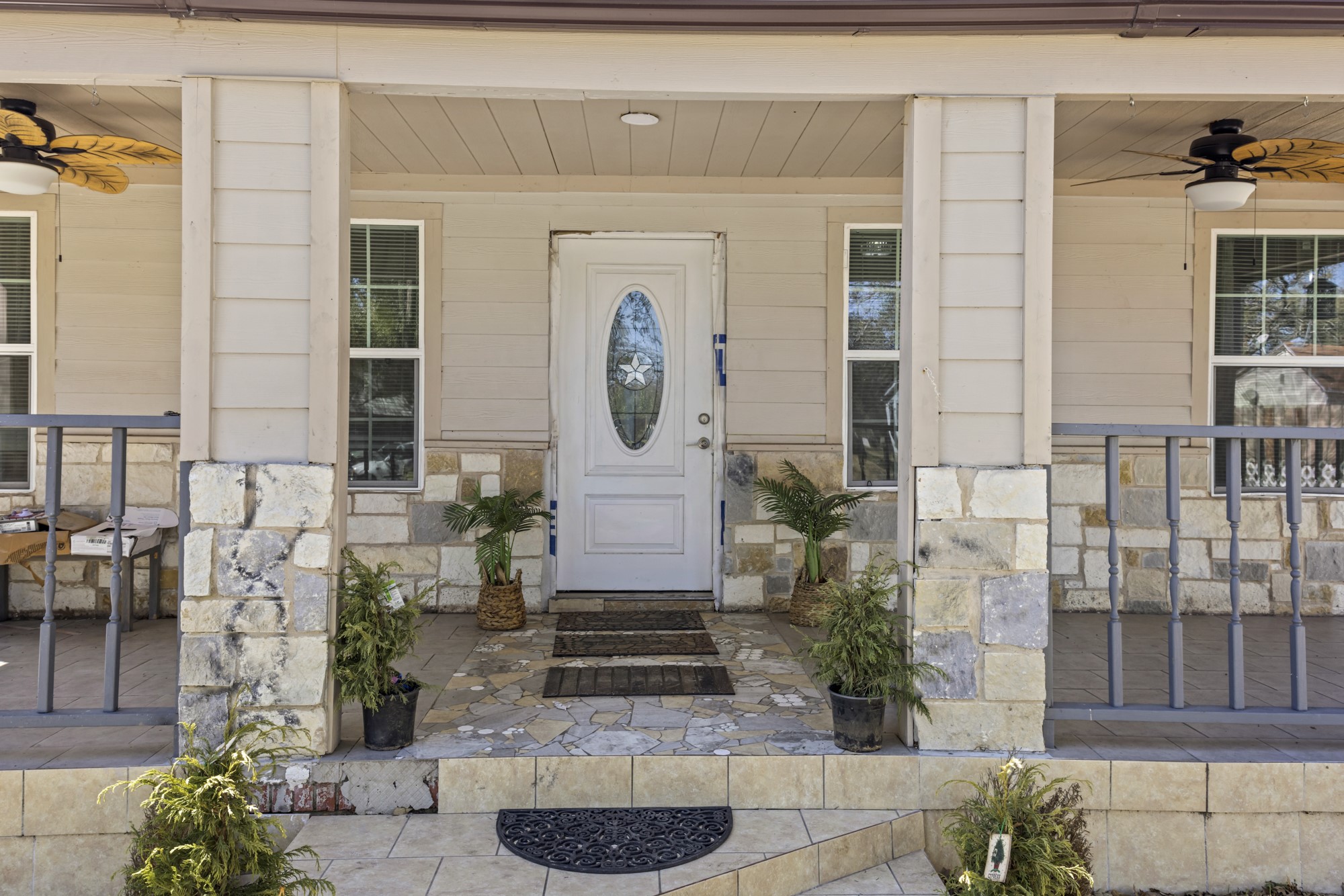 House entrance with a white oval-window door, stone columns, and a covered porch with potted plants.