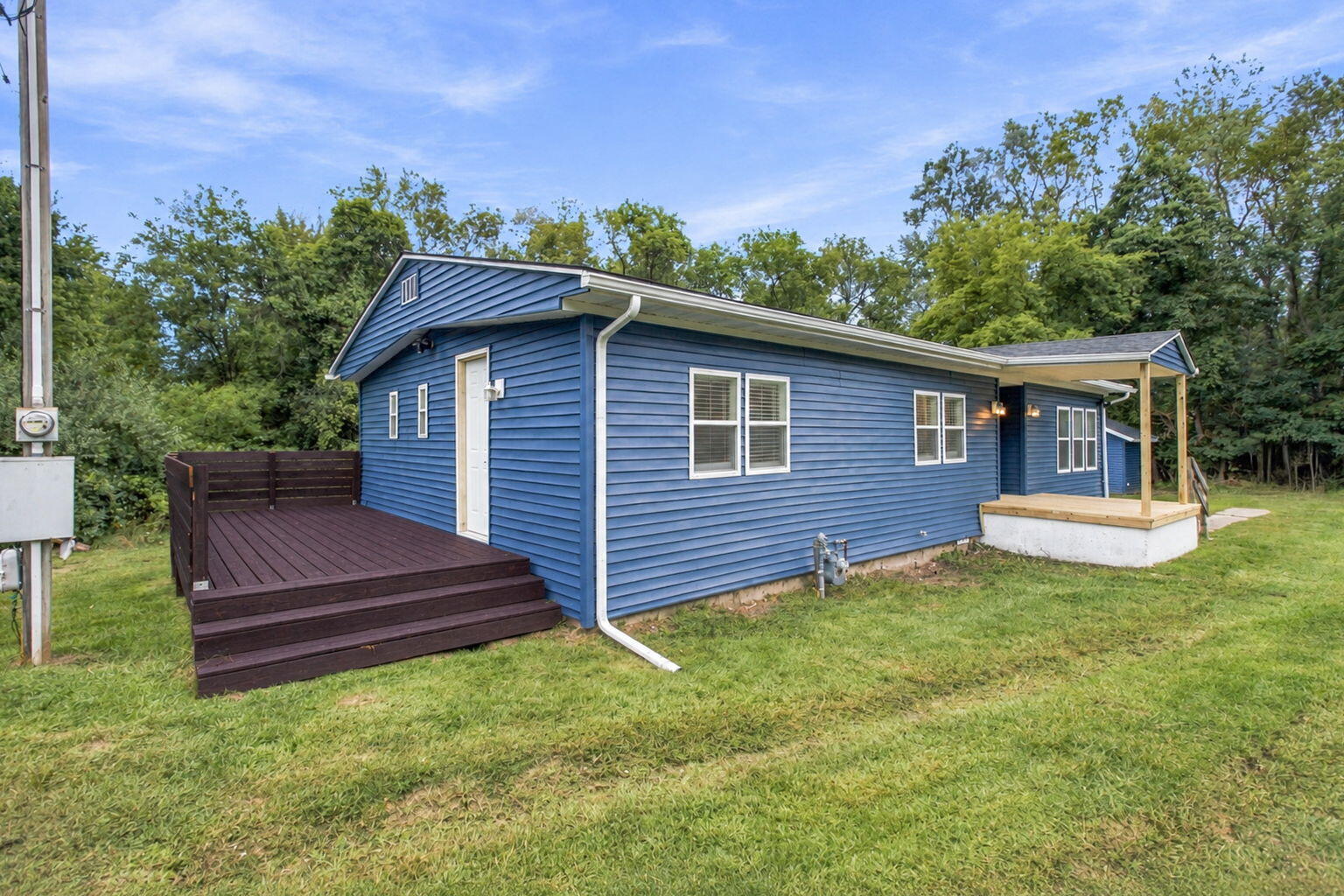 Blue-sided house with a dark wood deck and covered porch, surrounded by trees.
