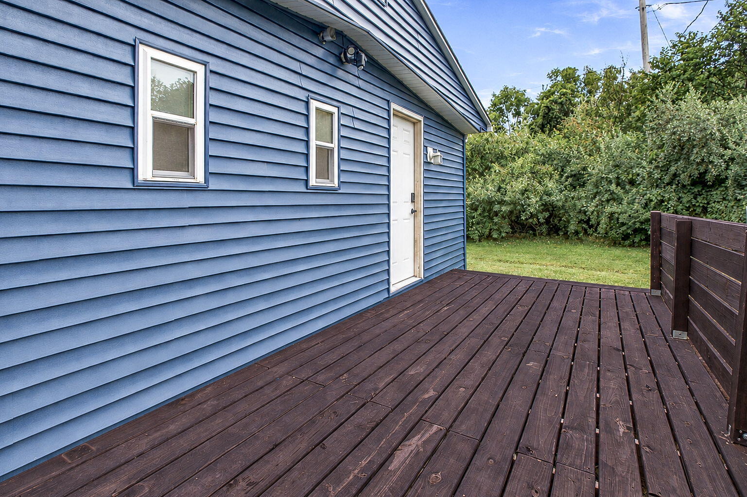Wood deck beside a blue-sided home, with a white door and fenced yard.