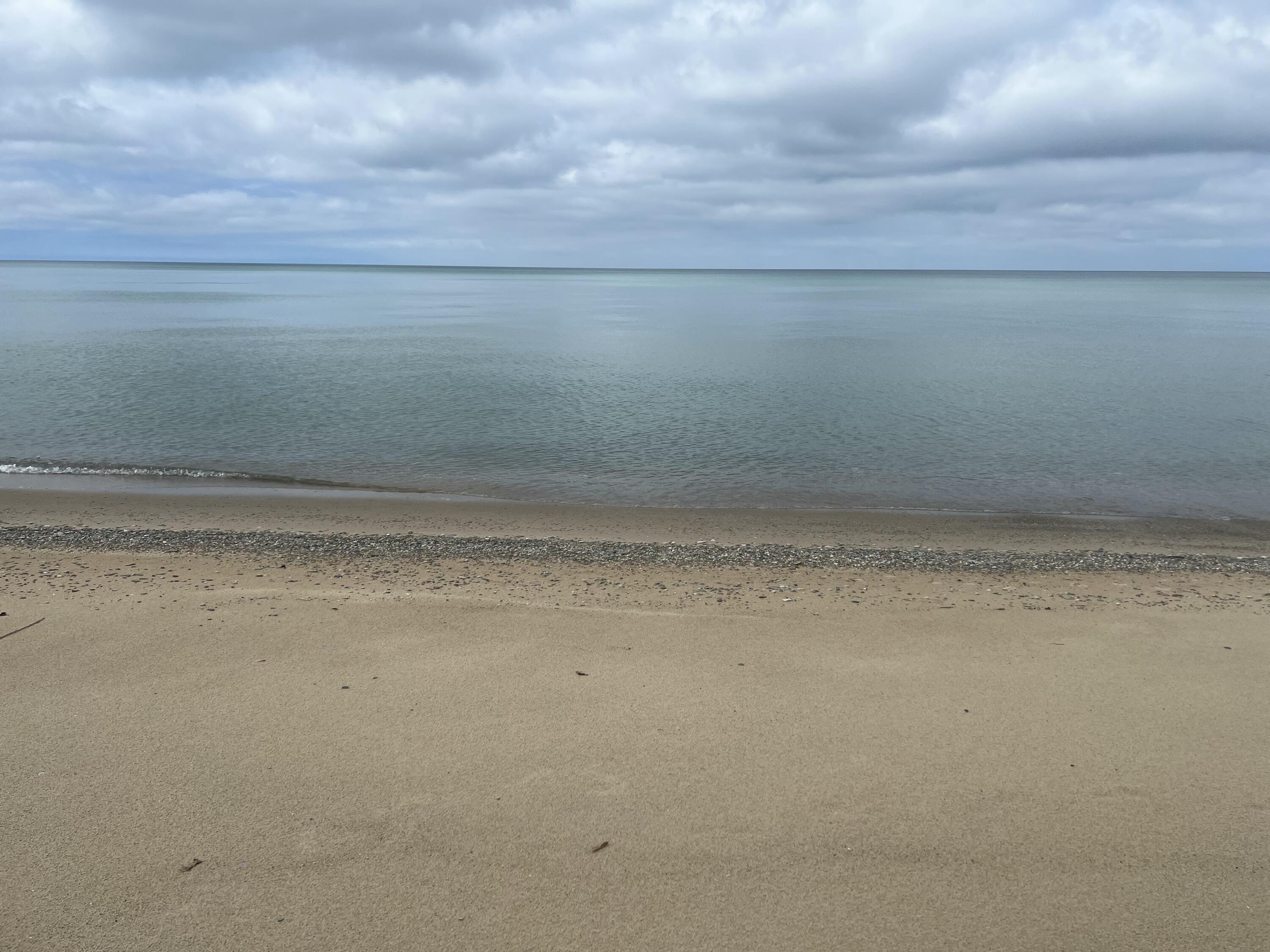 Sandy beach meets calm water beneath a cloudy sky.