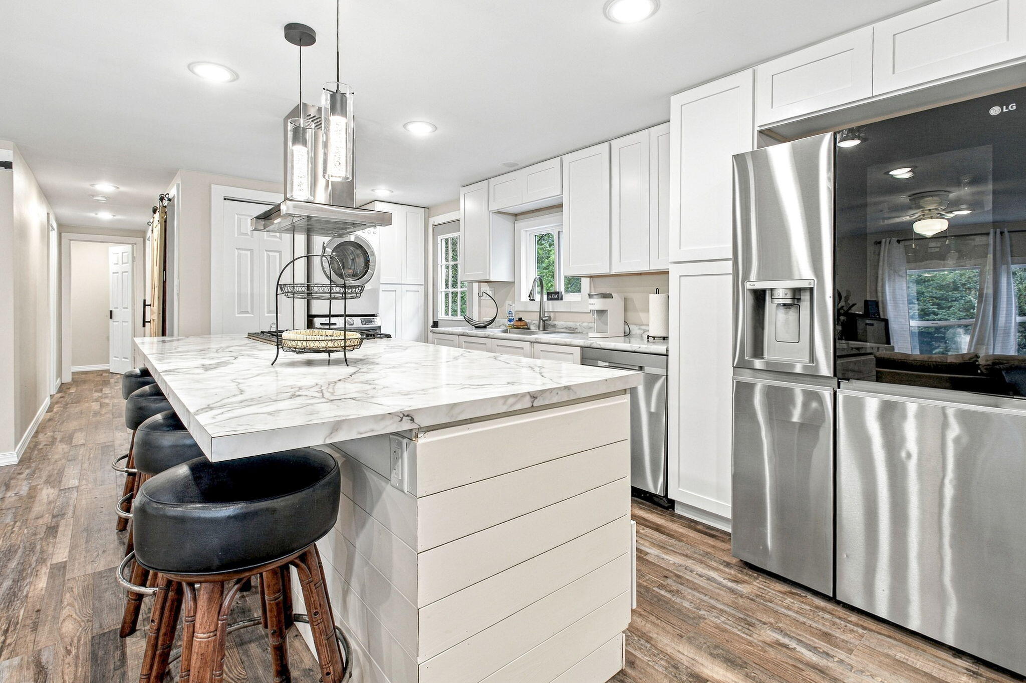 Kitchen with a large veined marble island, black bar stools, white cabinetry, and stainless steel appliances.