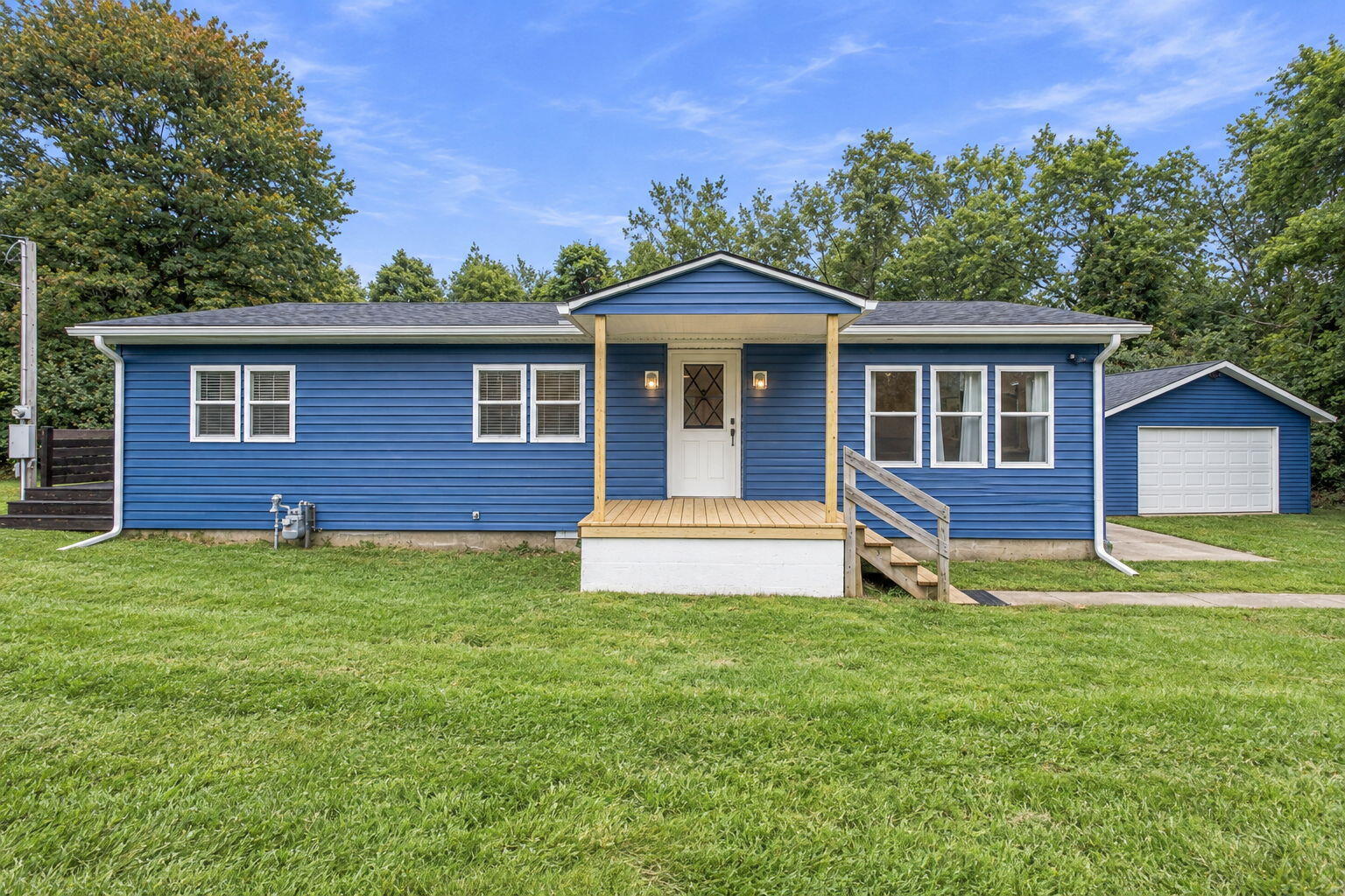 Blue single-story house with a raised wood porch and detached garage on a broad lawn.