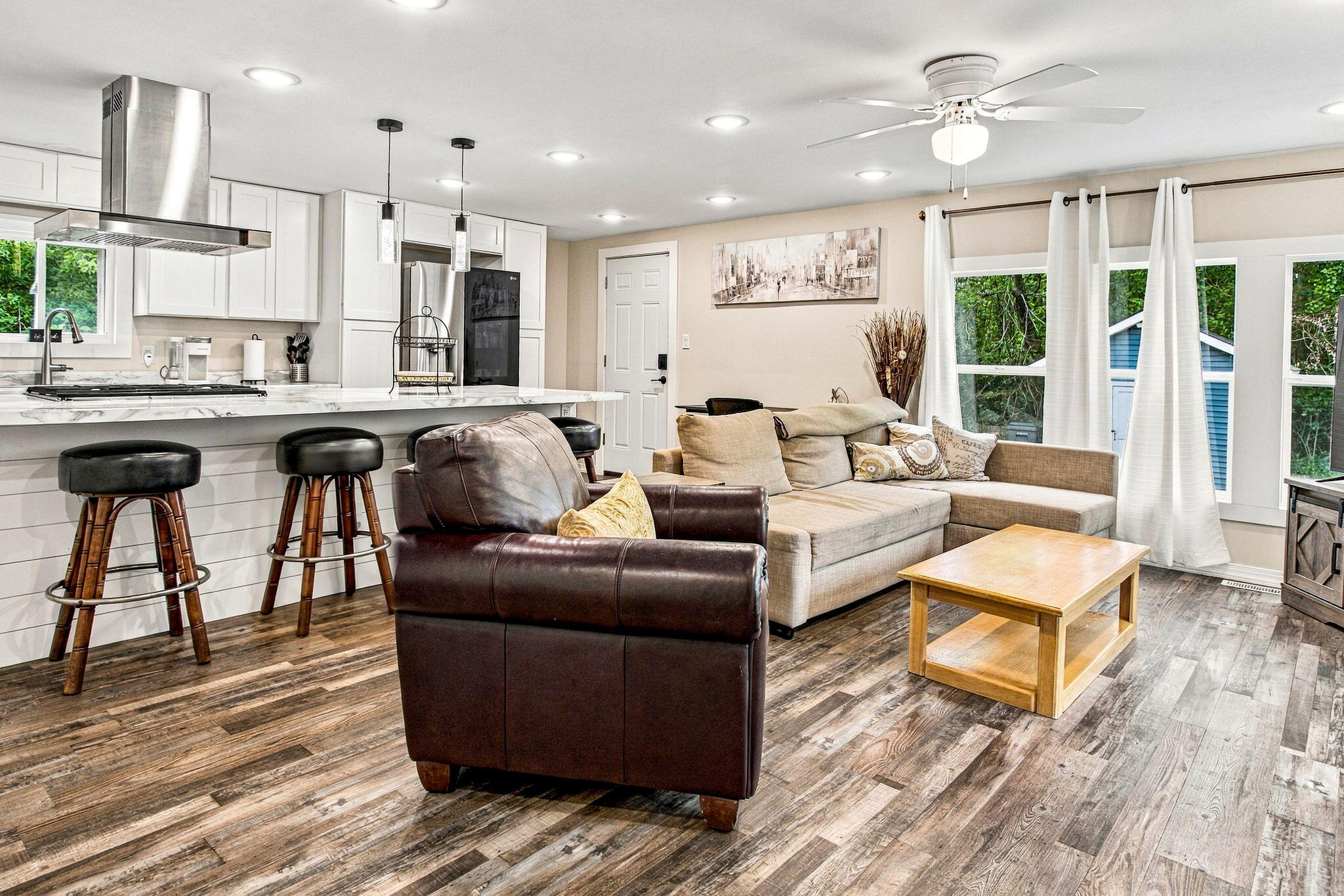 Open-plan living room and kitchen with a beige sectional, marble-look island, and rustic plank flooring.