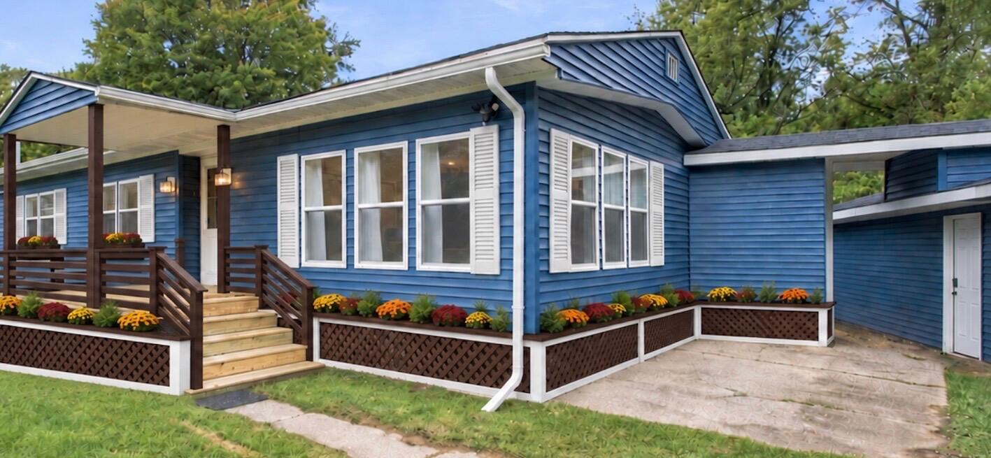 Blue-sided house with a covered porch, wooden steps, and colorful flower beds.