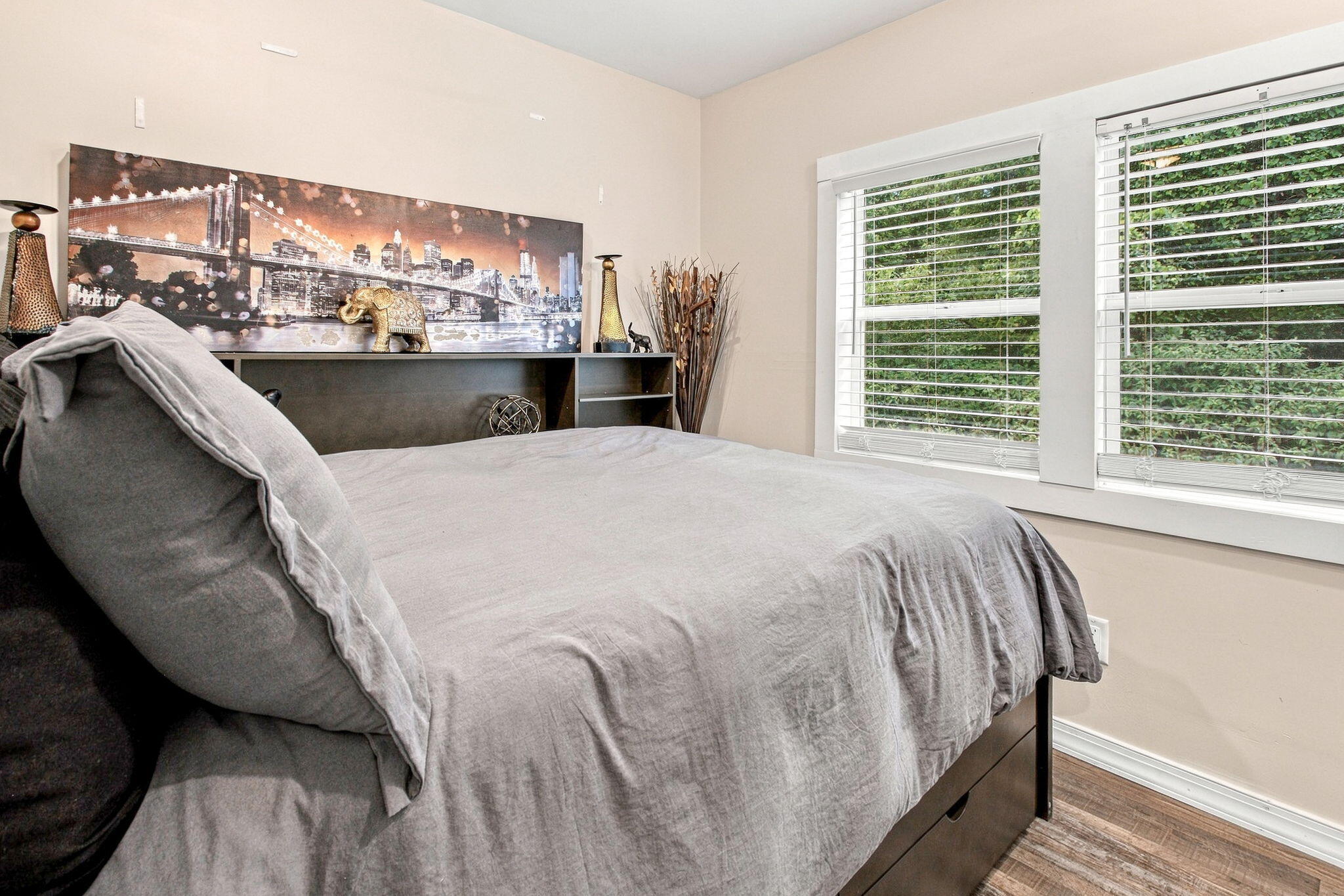Bedroom with gray bedding, wide windows, and cityscape artwork above the headboard.