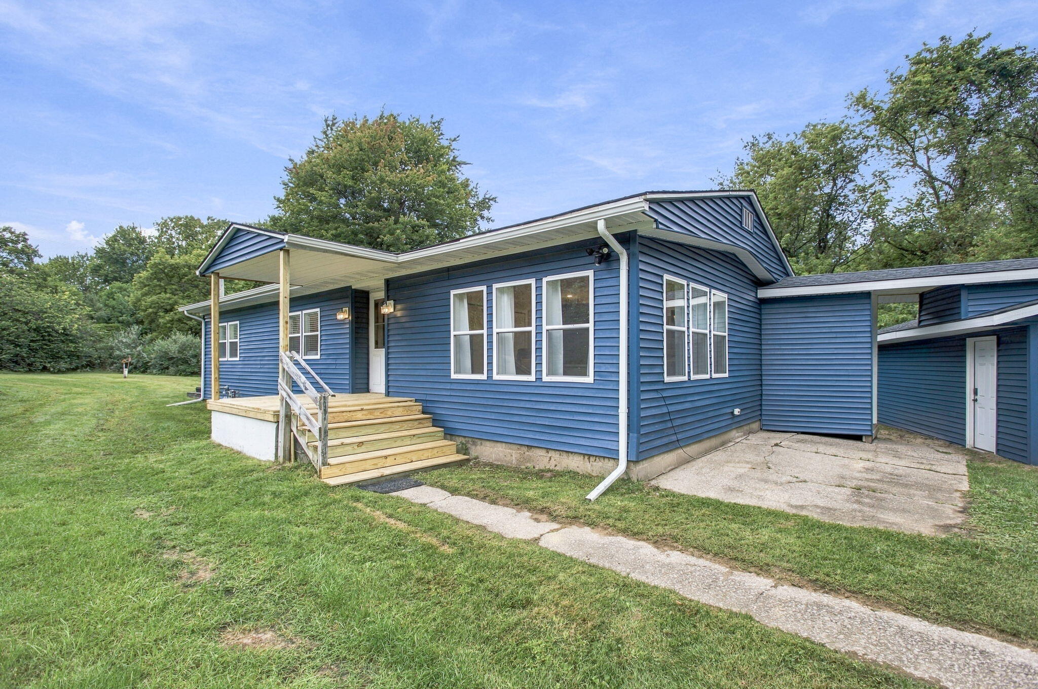 Blue-sided house with a covered porch, wooden steps, and an attached outbuilding.