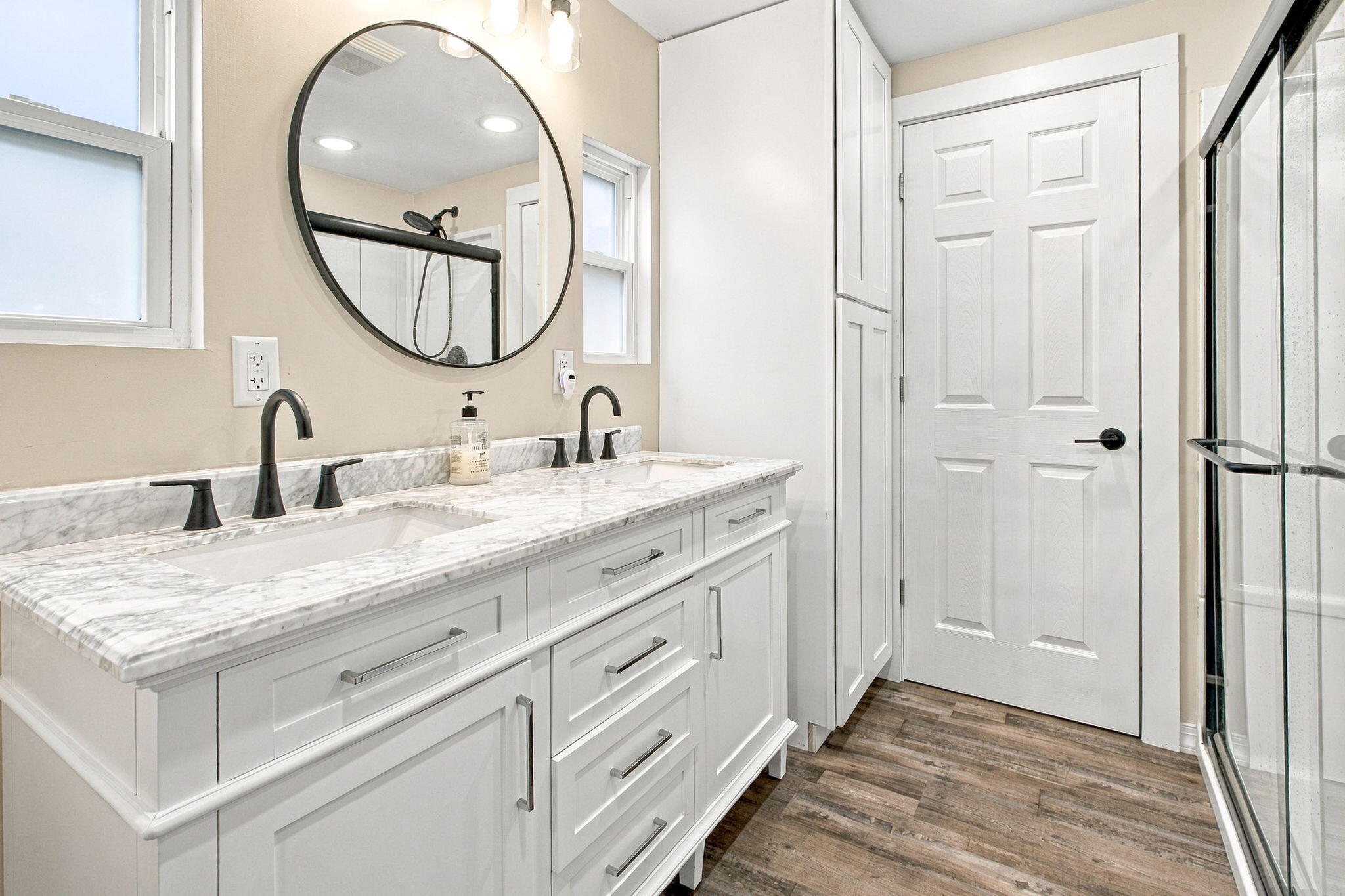 Bathroom with a white double vanity, marble-look countertop, round mirror, and glass shower.