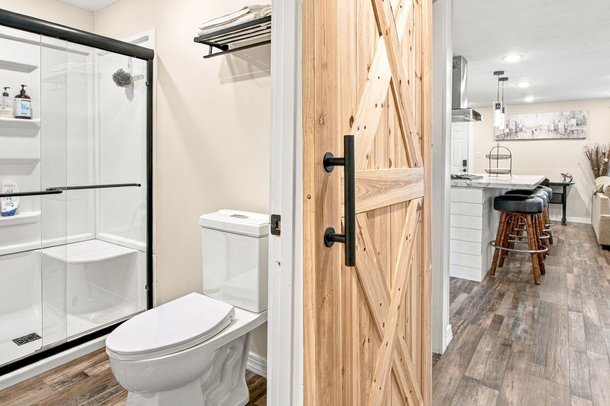 Bathroom with a glass shower and wood barn door opening toward a kitchen island.