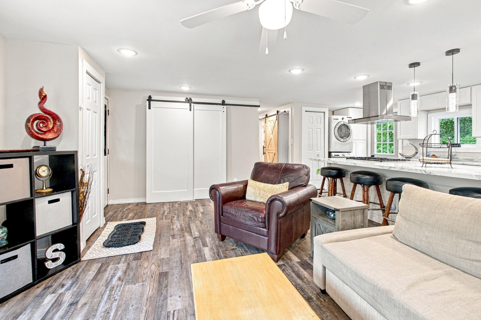 Open-plan living room and kitchen with a marble-look island, brown leather armchair, and sliding barn doors.