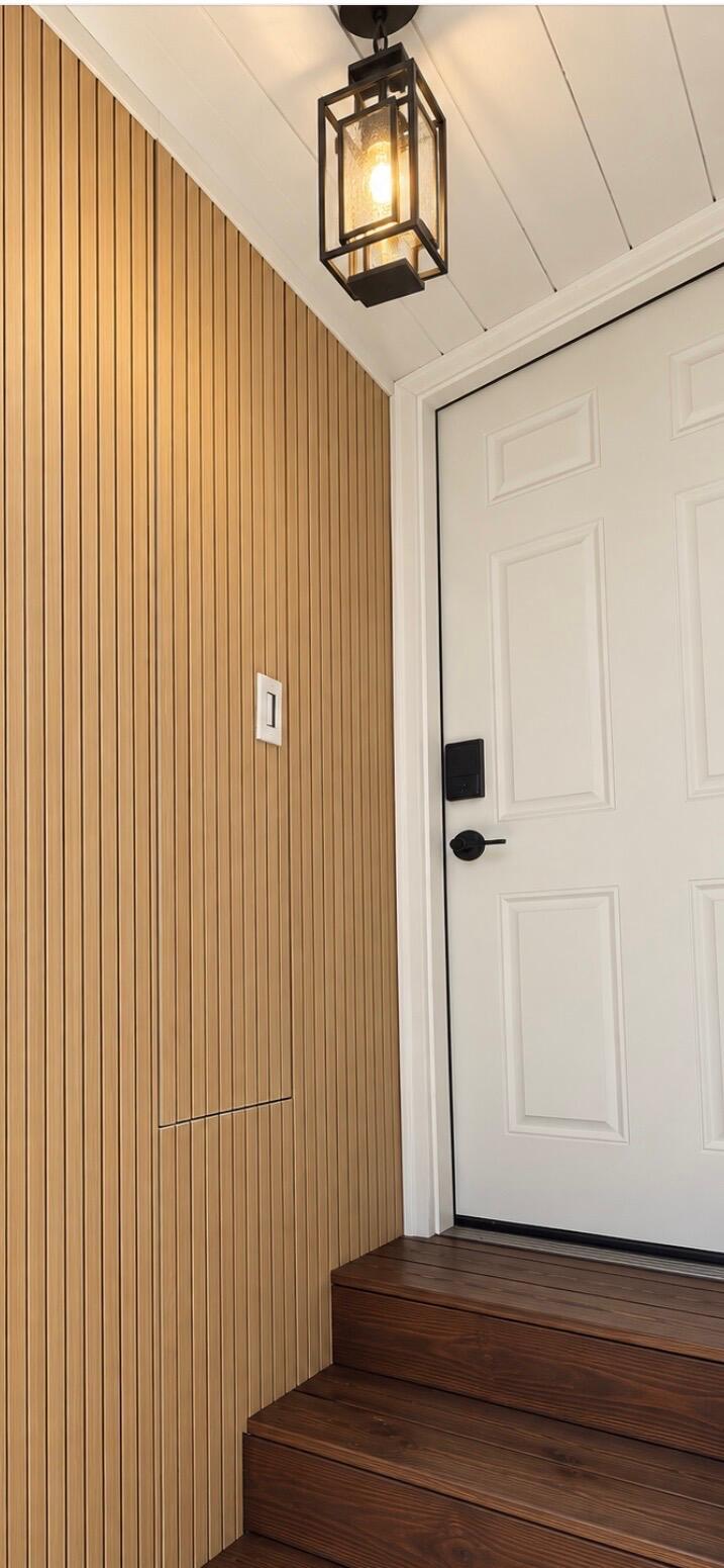 Entryway with a white paneled door, wood slat wall, dark steps, and black lantern.