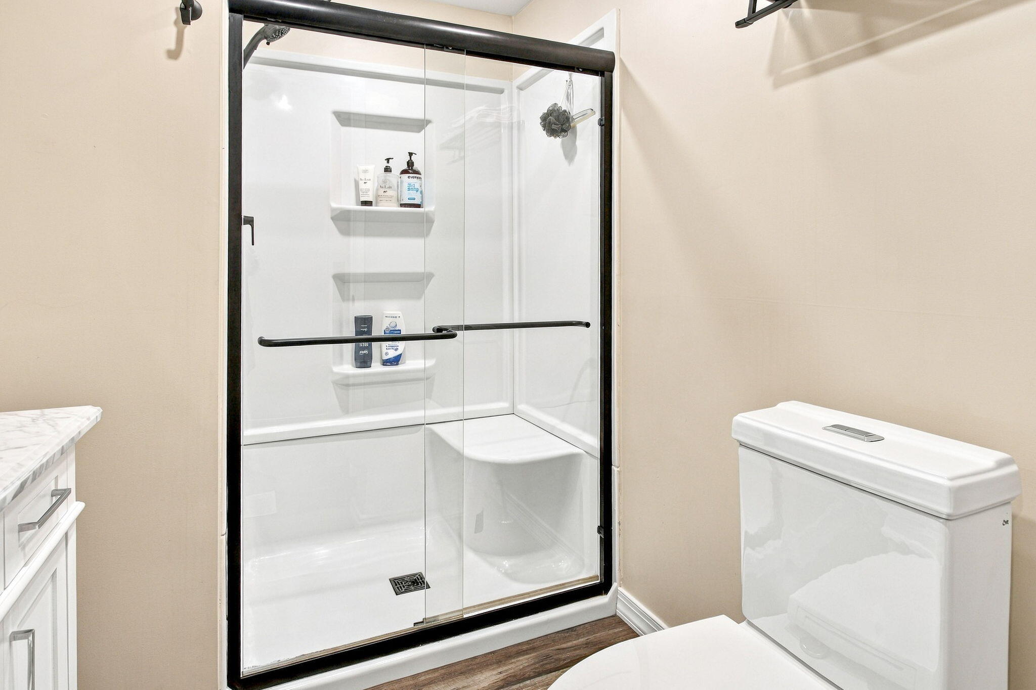Bathroom with a black-framed glass shower, built-in shelves, white toilet, and dark wood flooring.