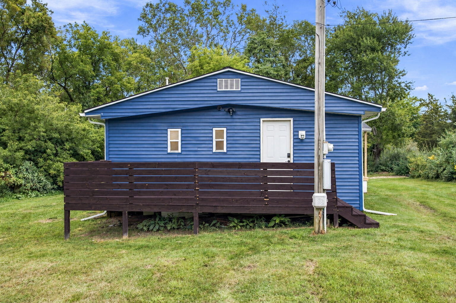Blue house with a raised dark-wood deck, white door, and utility pole in the foreground.