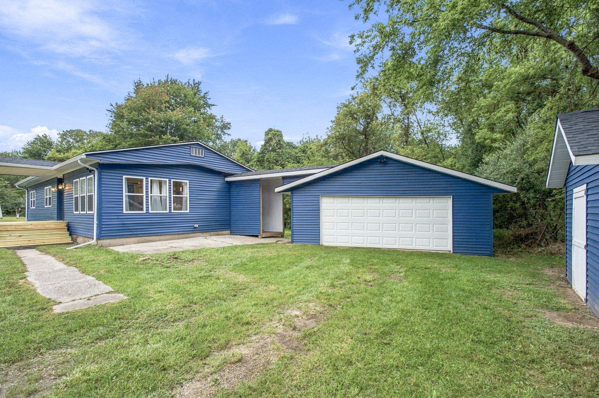 Blue-sided home and white two-car garage beside a grassy yard and mature trees.