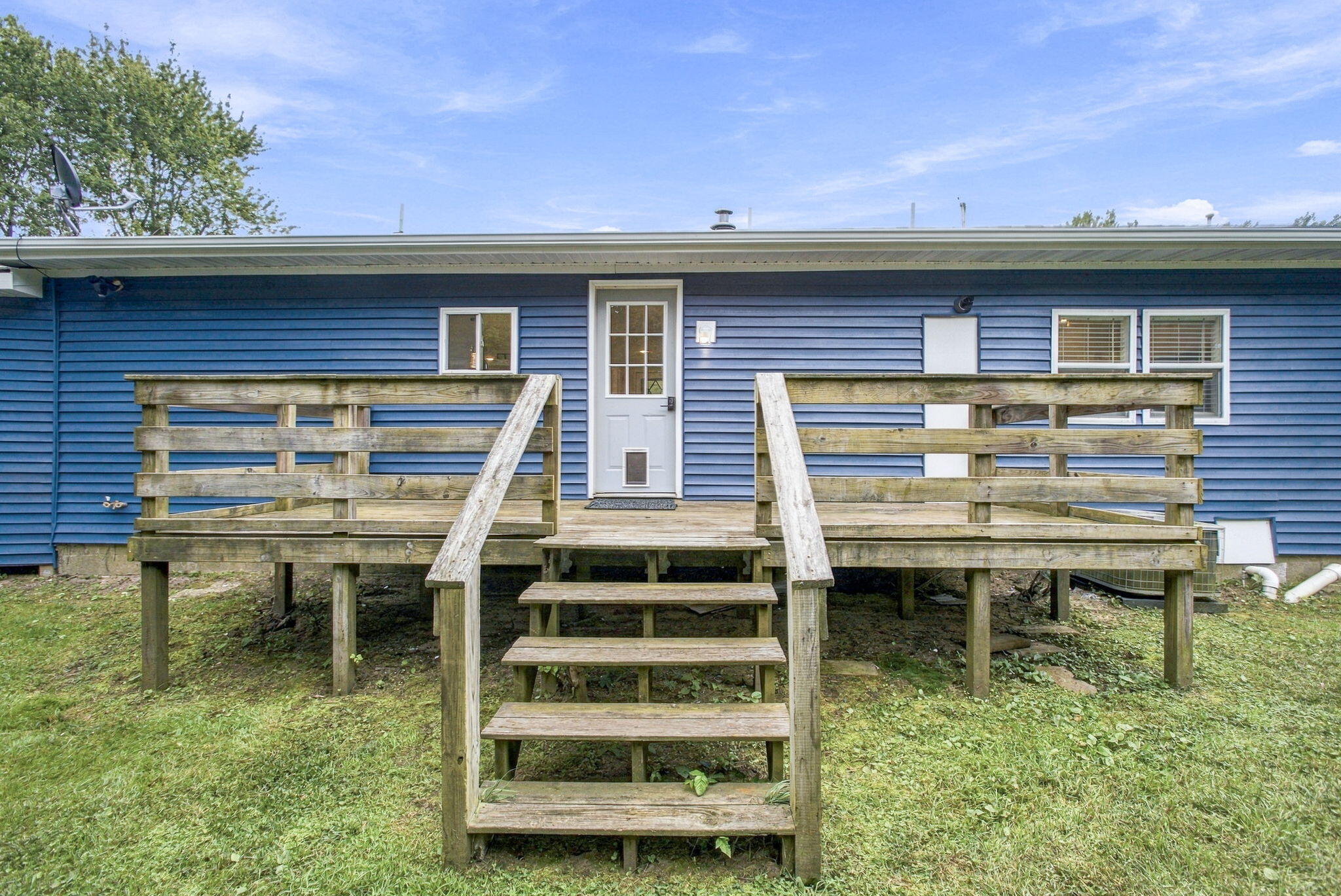 Blue-sided house with a raised wooden deck and central stairs leading to a white door.