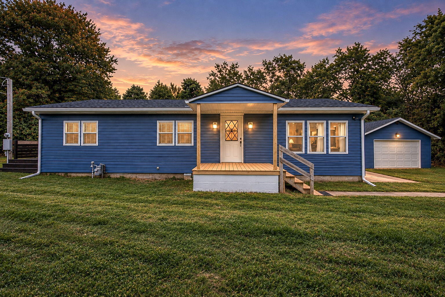 Blue single-story home with a covered porch and detached garage at sunset.