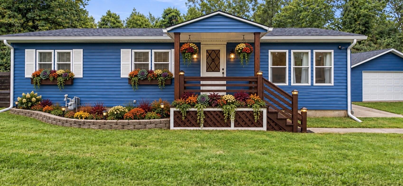 Blue single-story house with a raised wooden porch, colorful flower boxes, and a landscaped front garden.