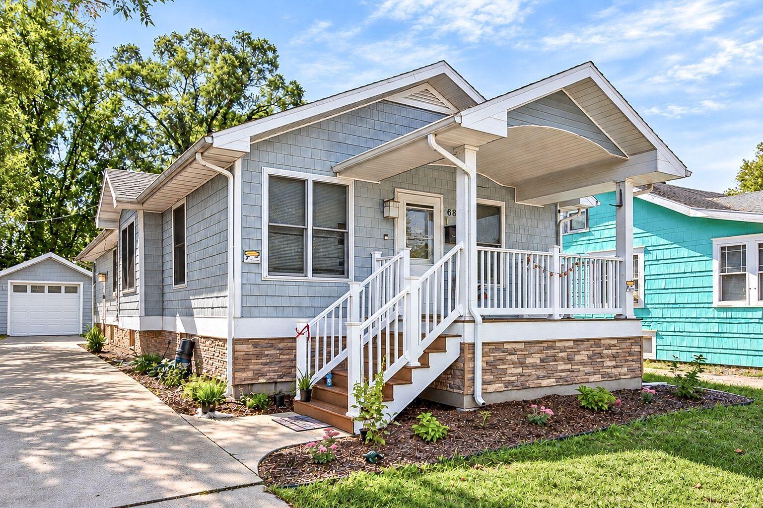 Blue-gray shingle-sided home with a covered porch, white railings, front steps, and detached garage.