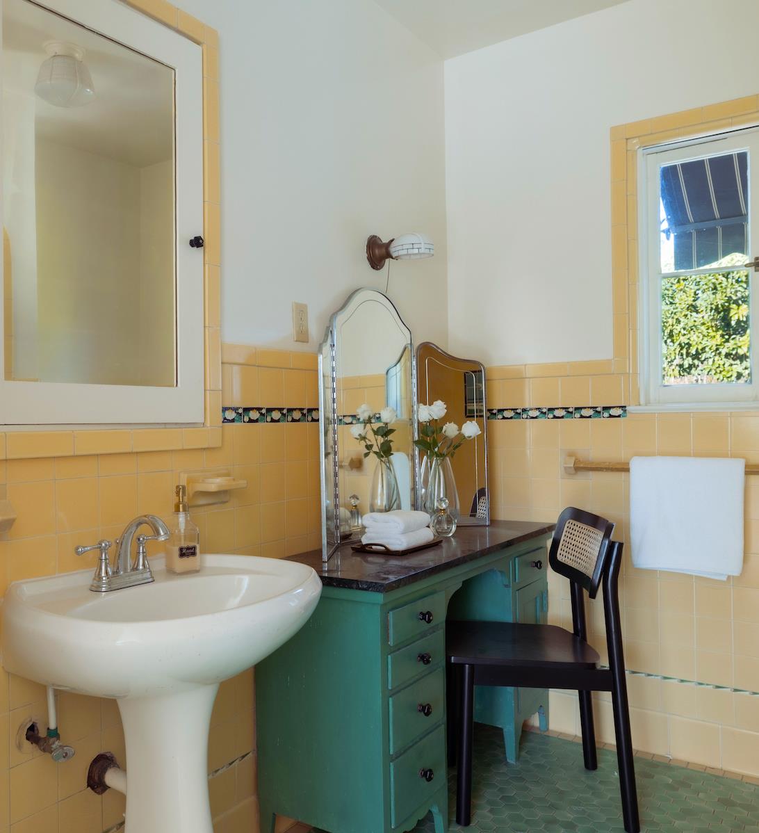 Bathroom with yellow tile, a white pedestal sink, and a green vanity beneath mirrors.