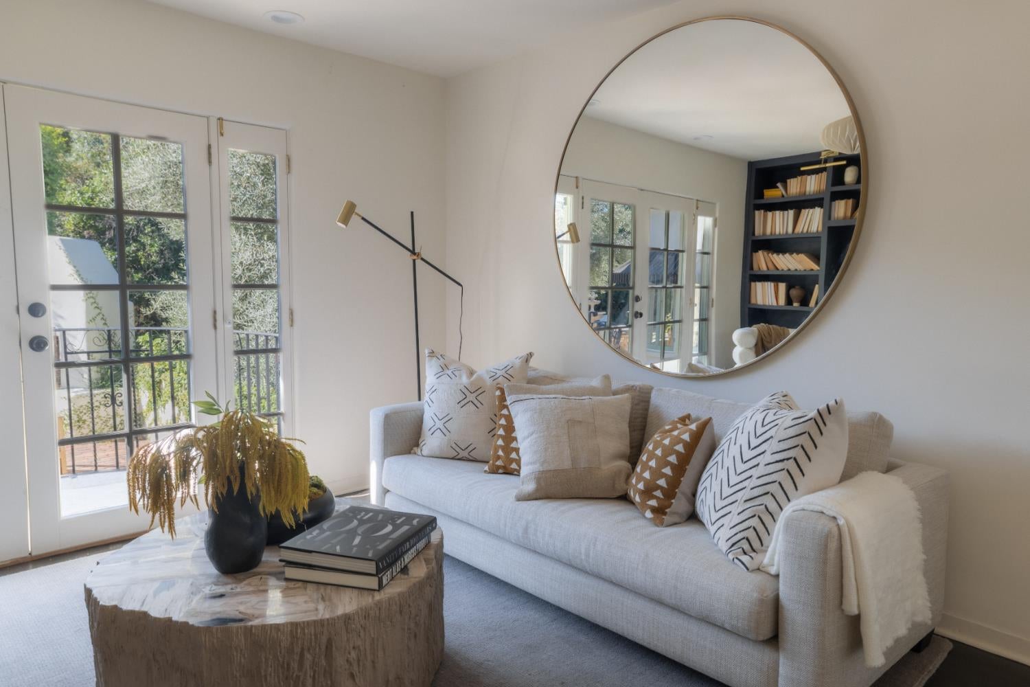 Furnished living room with a light sofa, French doors, and a large round mirror.