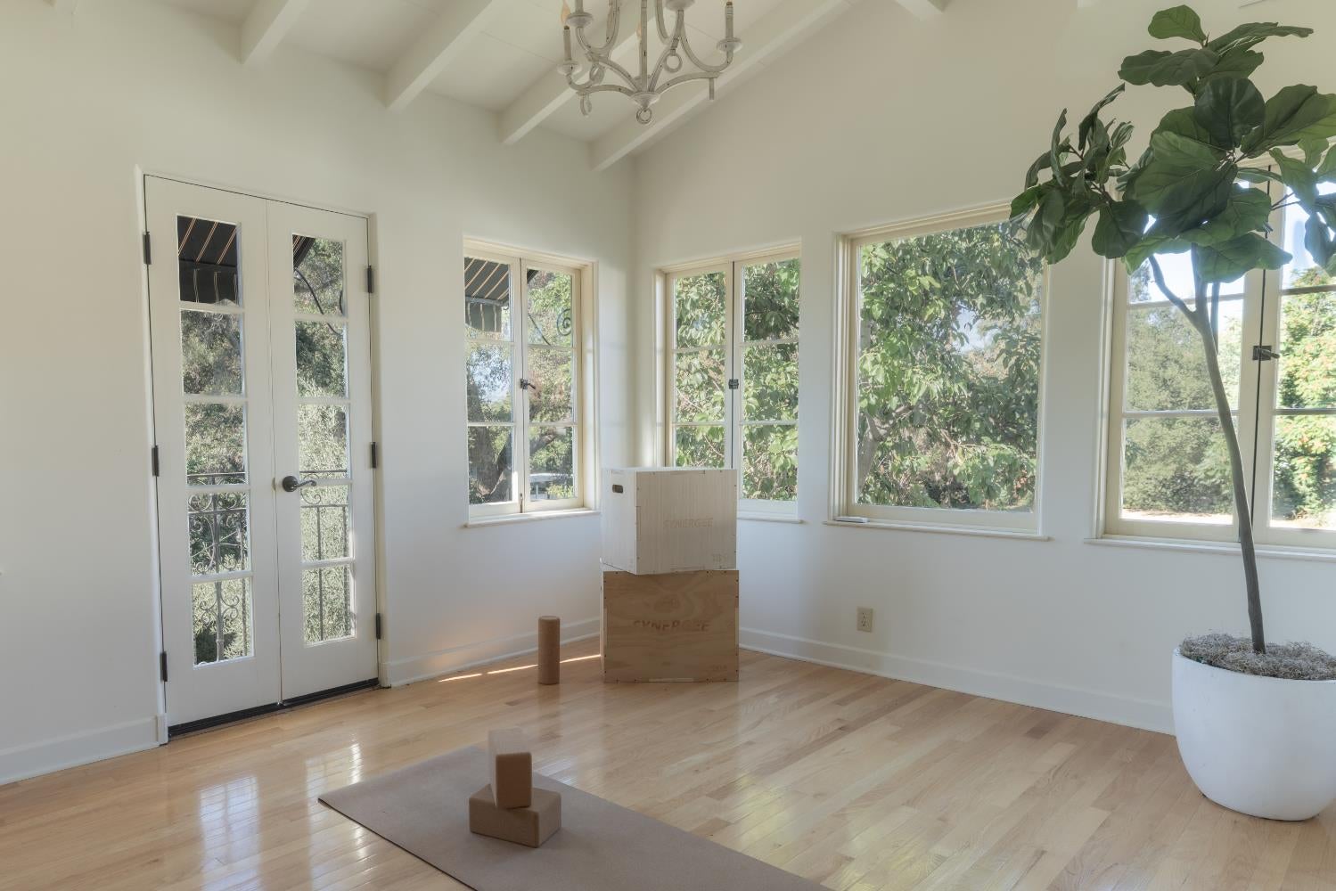 Bright room with hardwood floors, a beamed ceiling, and large windows overlooking trees.