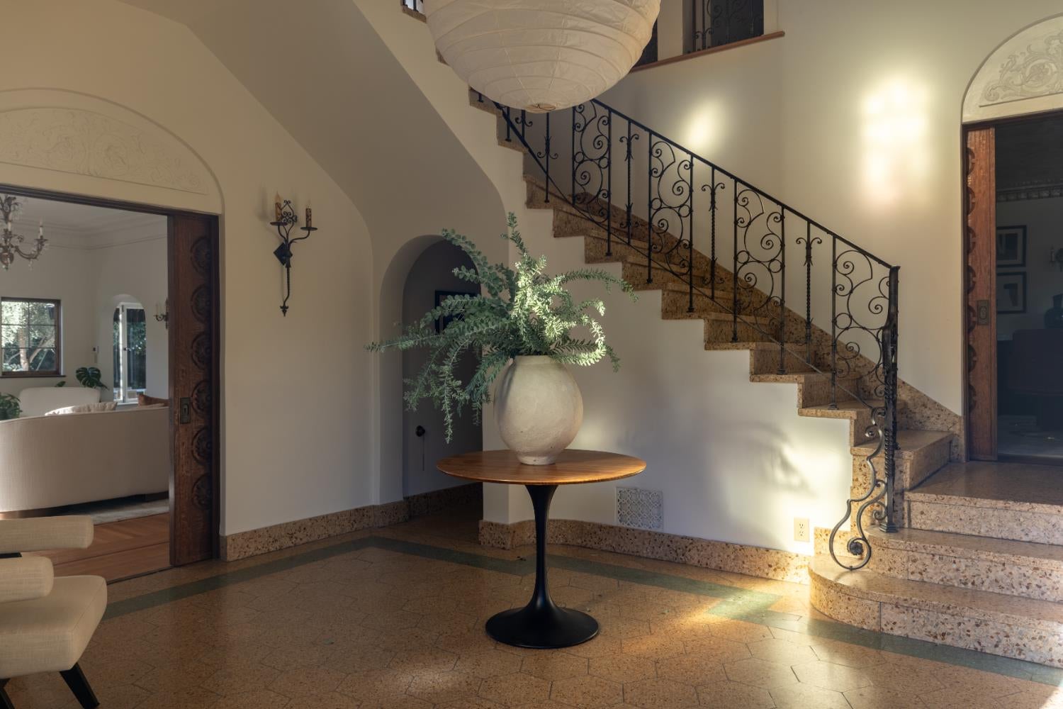 Foyer with a curved stone staircase, wrought-iron railing, and round table topped with a leafy vase.
