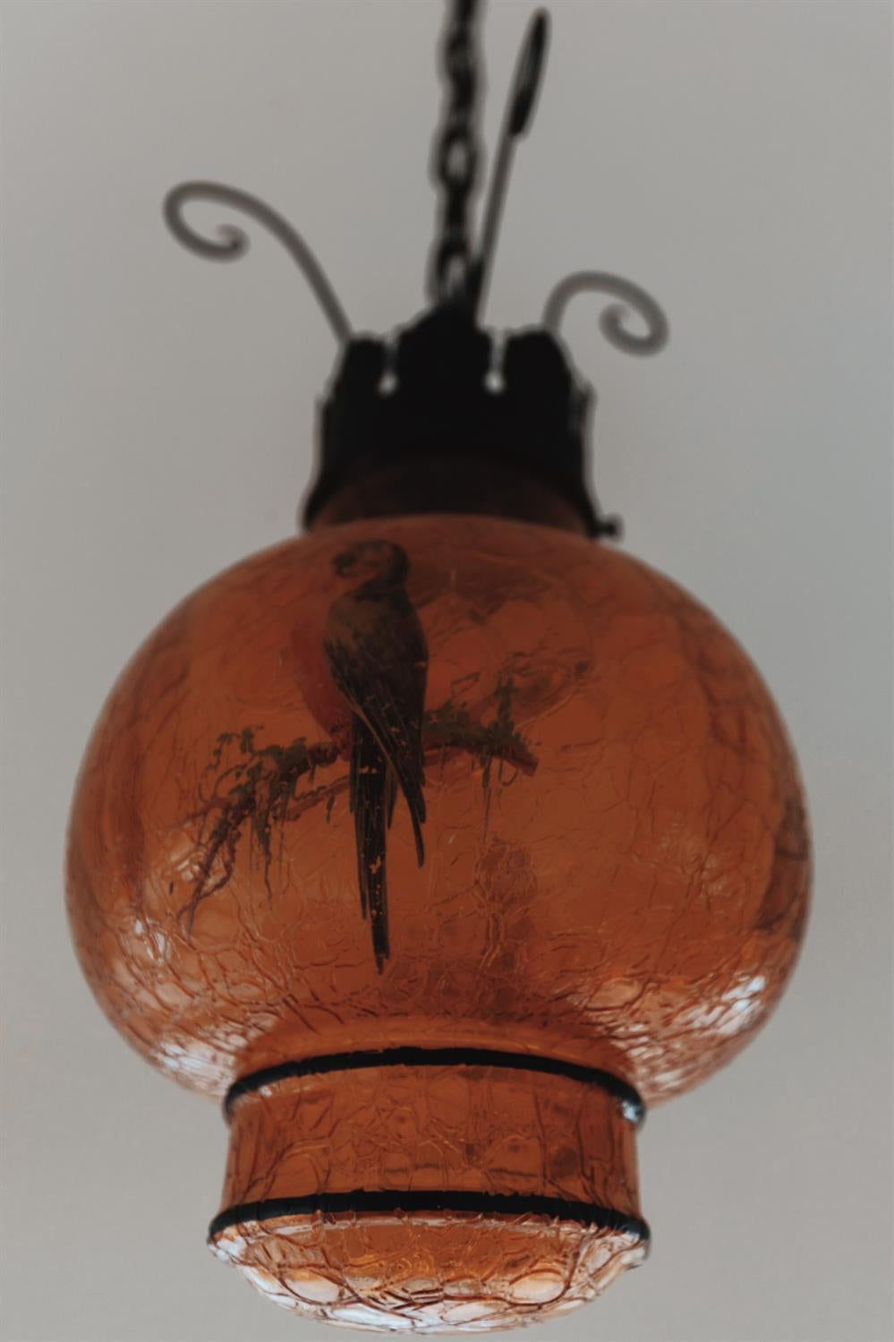 Amber glass pendant light with a textured globe and bird-and-branch motif.