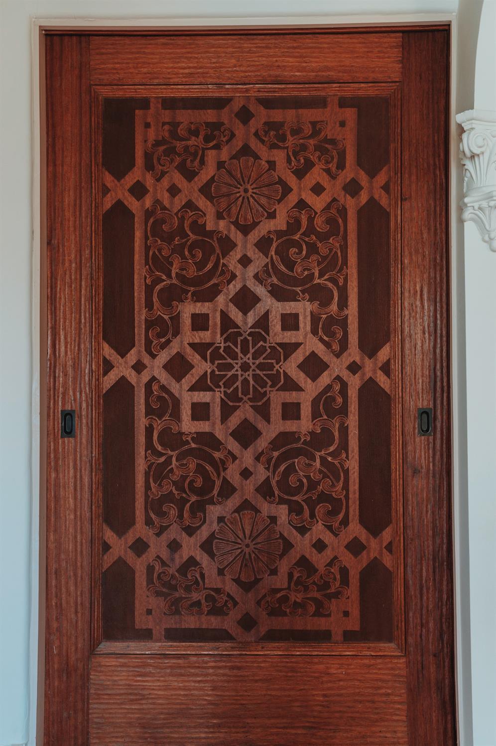 Ornately carved wooden door with geometric and floral details and recessed handles.