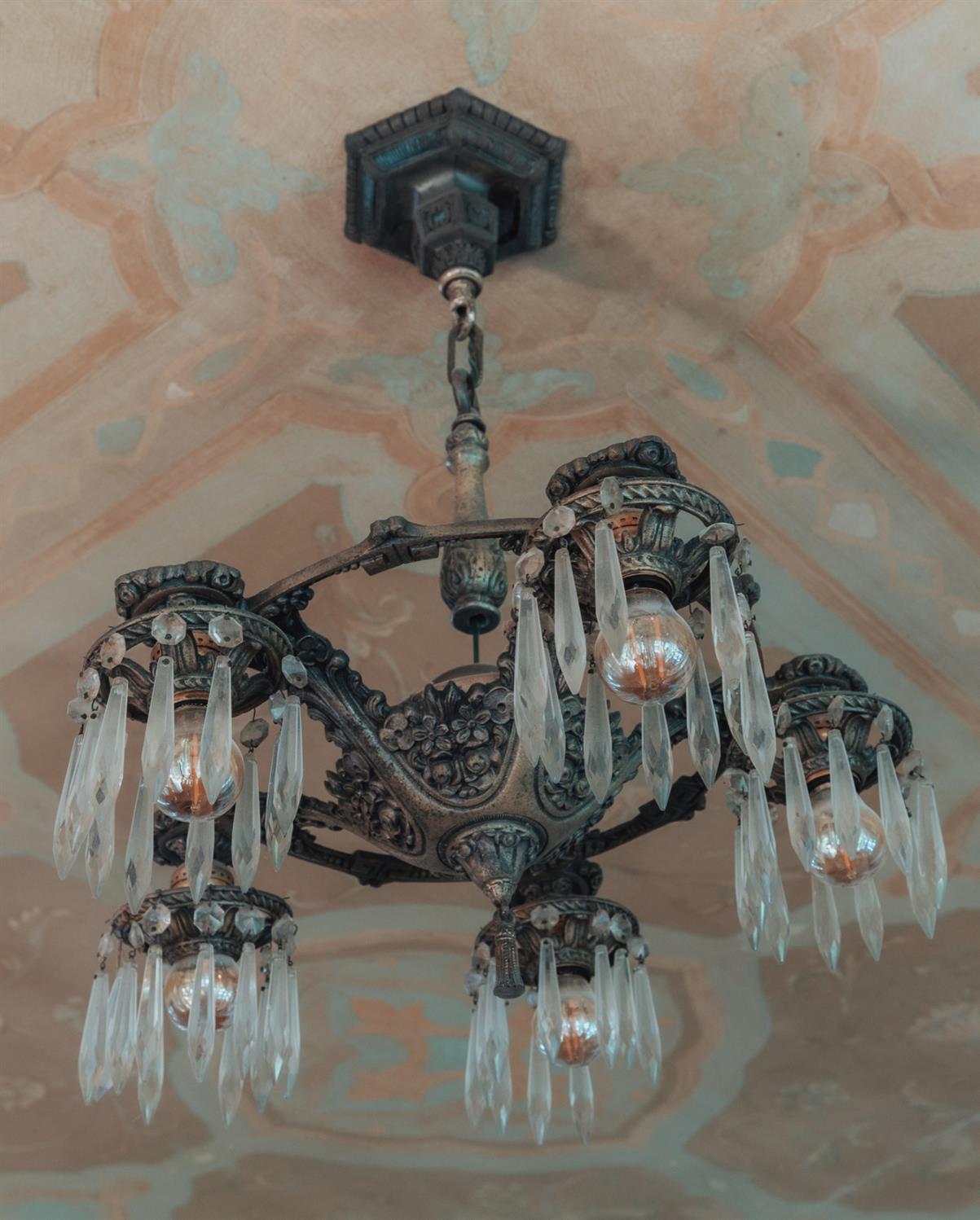 Ornate chandelier with crystal drops beneath a peach-and-blue patterned ceiling.