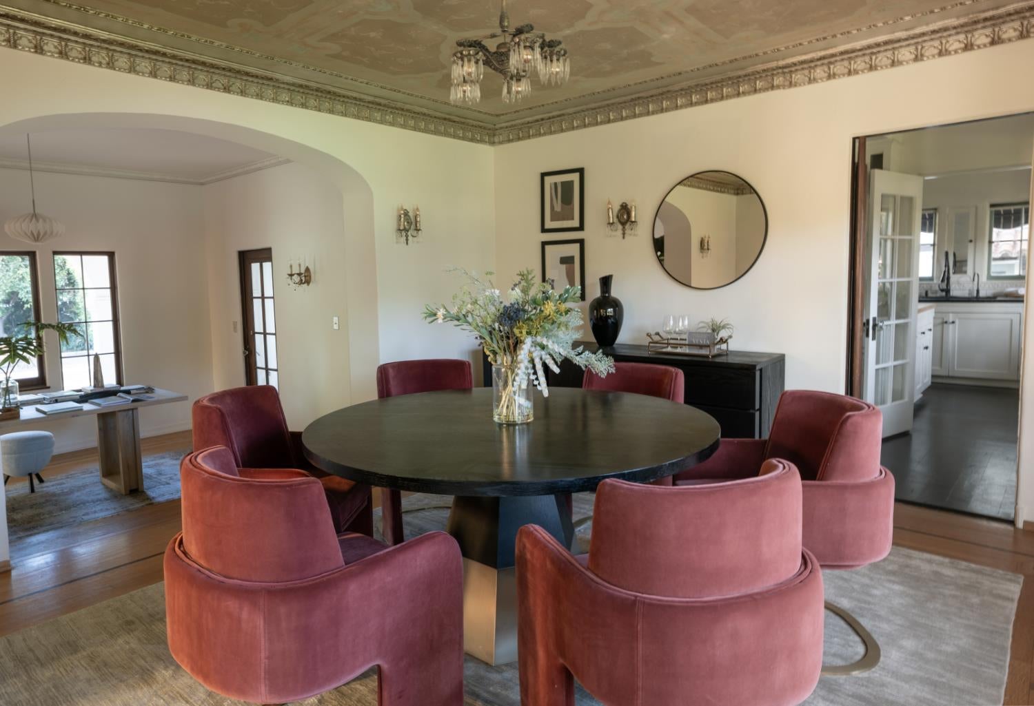 Dining room with a round table, rust-colored chairs, and ornate ceiling beside an arched opening.