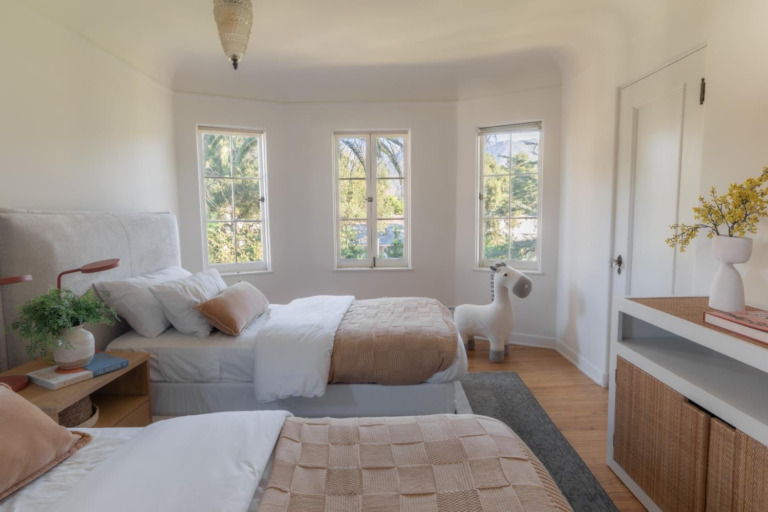 Bright bedroom with two beds, tall windows, and distant mountains visible outside.