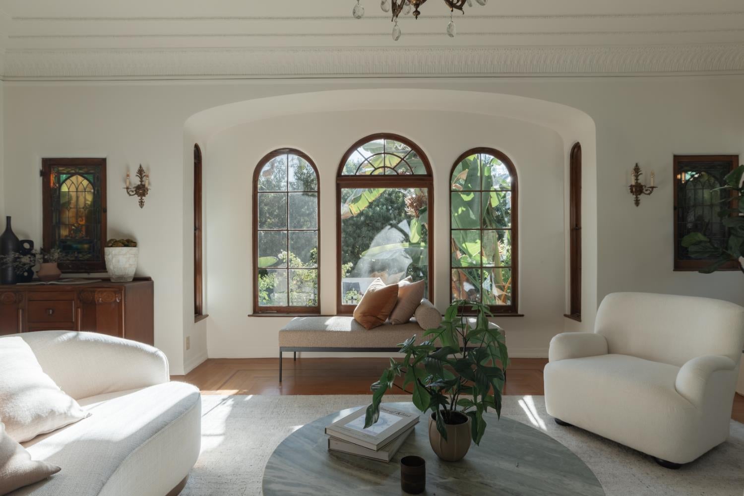 Furnished living room with arched garden-facing windows and white seating.