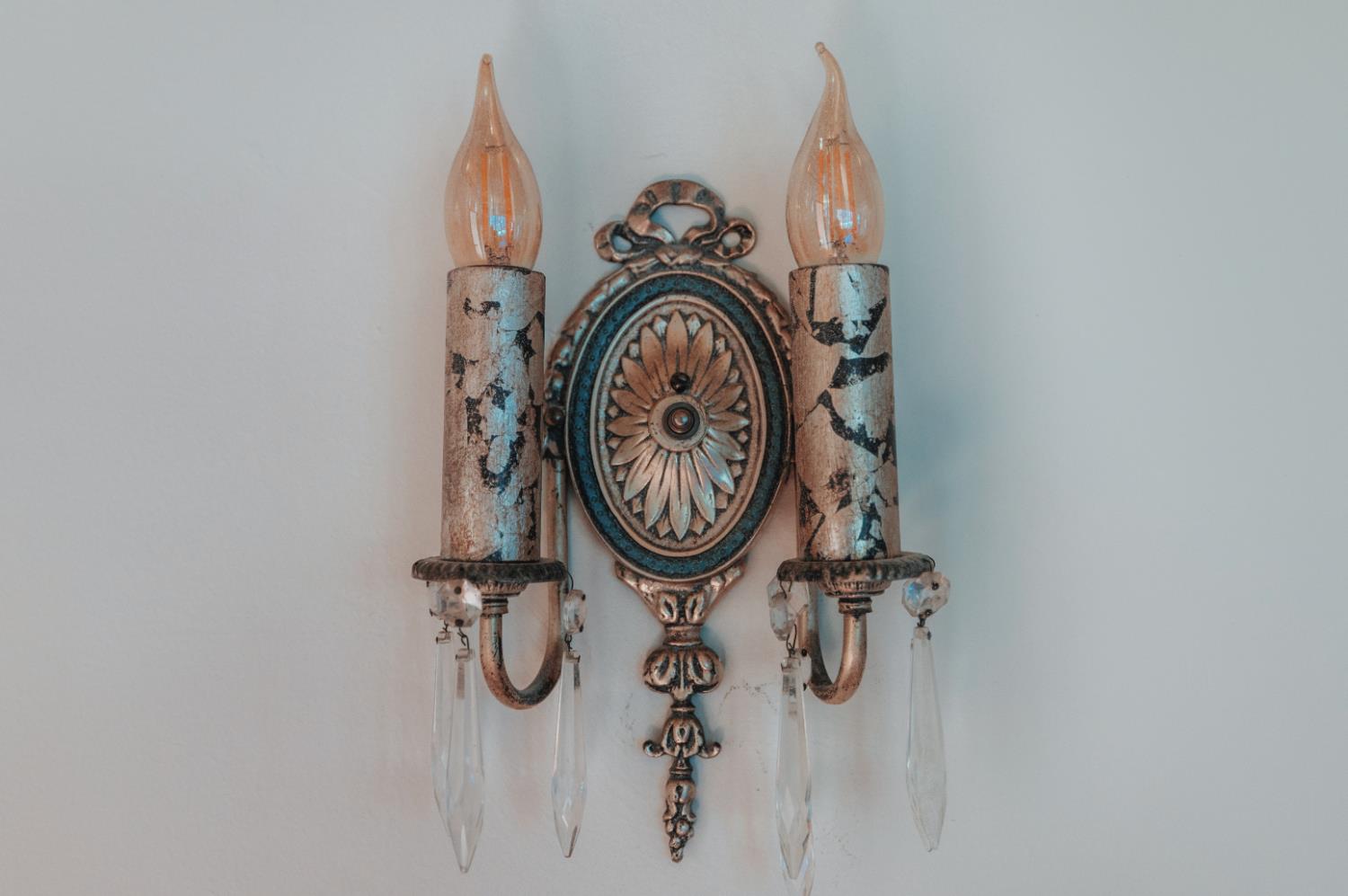 Ornate double wall sconce with a distressed finish and hanging crystal drops.