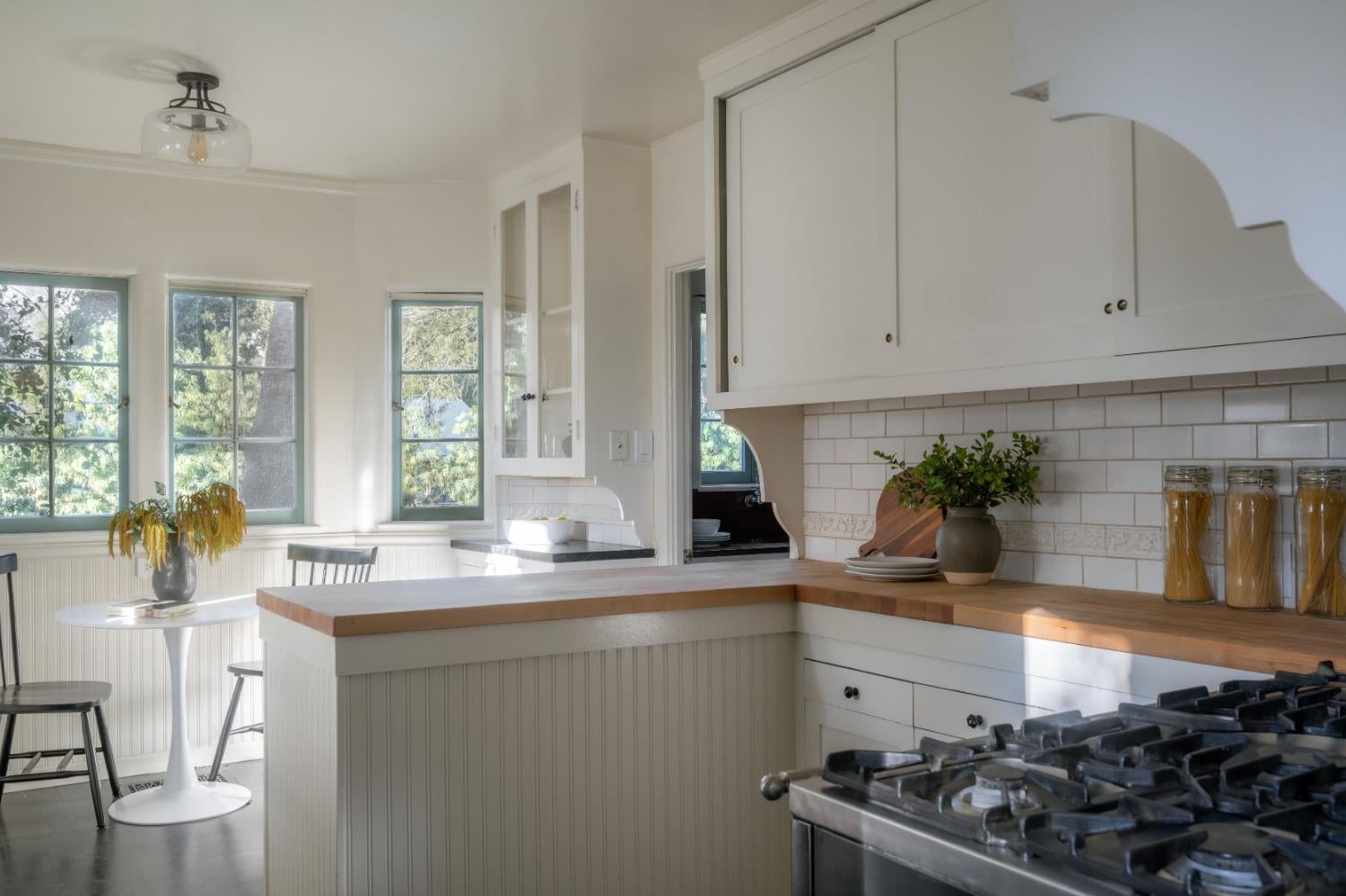 Kitchen with a wood-topped island, white cabinets, and a gas range beside tall windows.