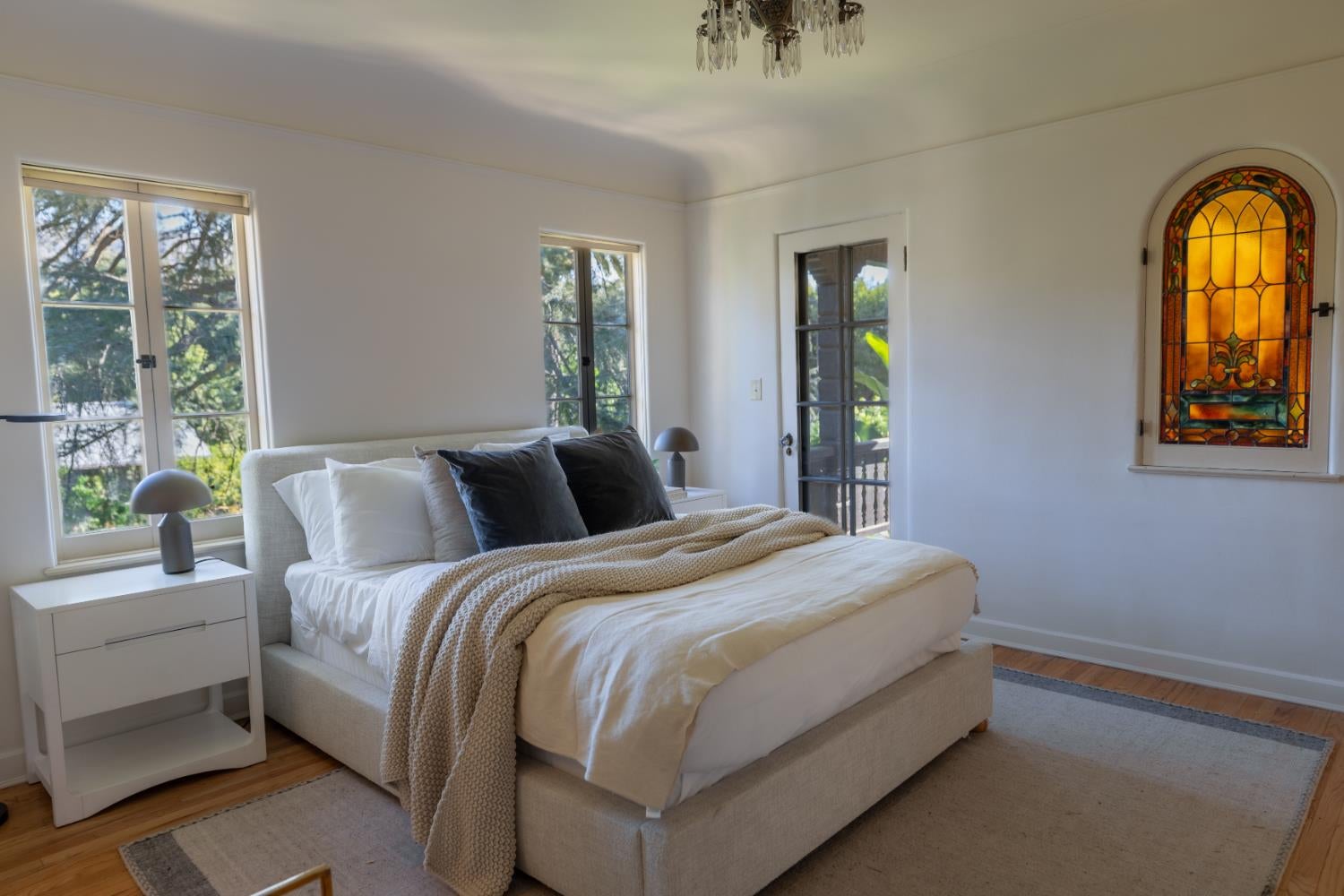 Staged bedroom with a cream bed, large windows, and an amber stained-glass window.