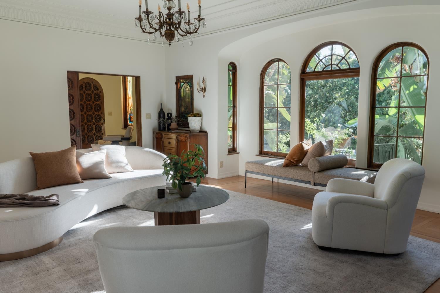 Living room with curved white sofas and tall arched windows overlooking greenery.