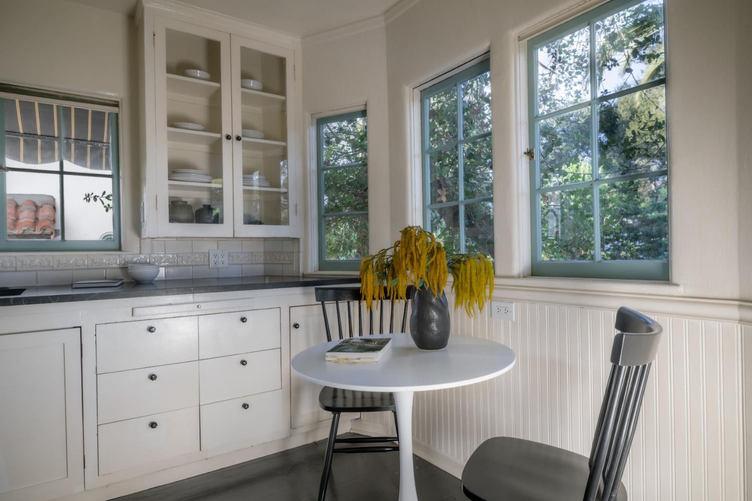 Kitchen breakfast nook with built-in cabinets, a round table, and large windows overlooking trees.