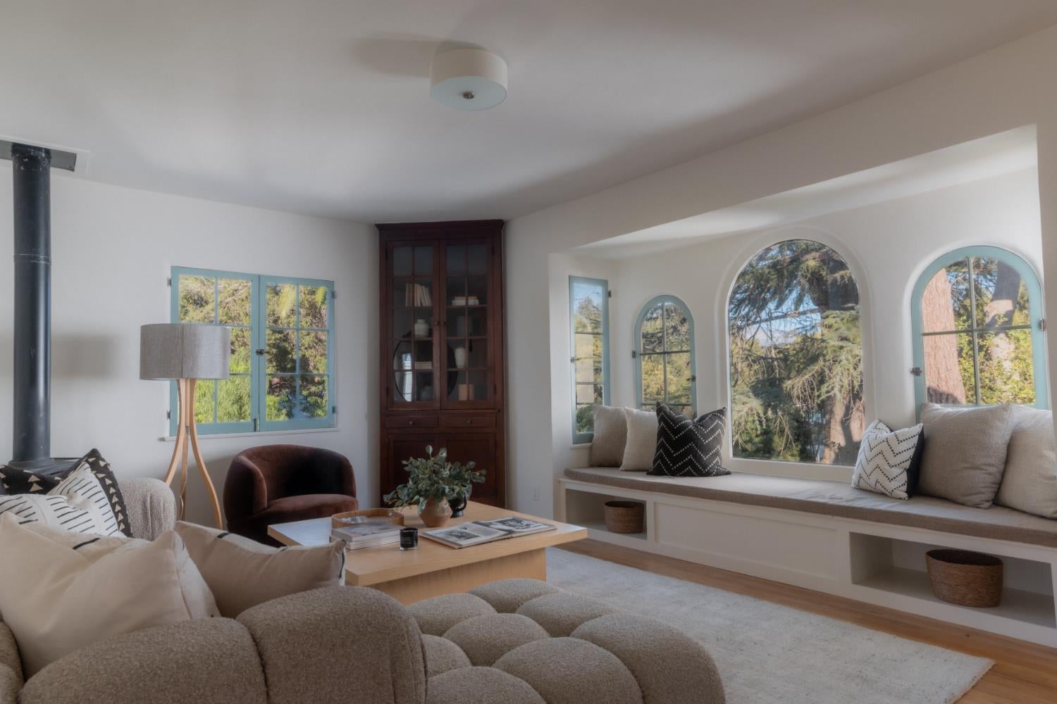Living room with a wood stove, built-in cabinet, and window seat beneath arched windows.