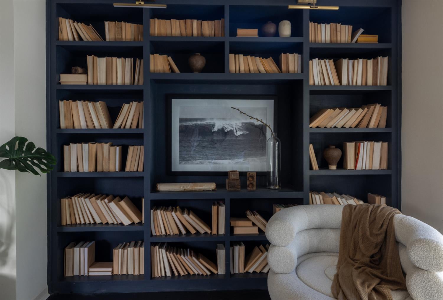 Living room with a navy built-in bookcase, ocean-wave artwork, and a white chair with a brown throw.