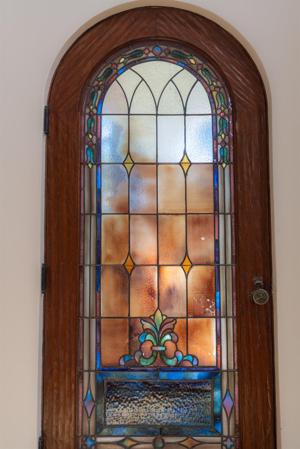 Arched wooden door with an ornate stained-glass panel and floral motif.