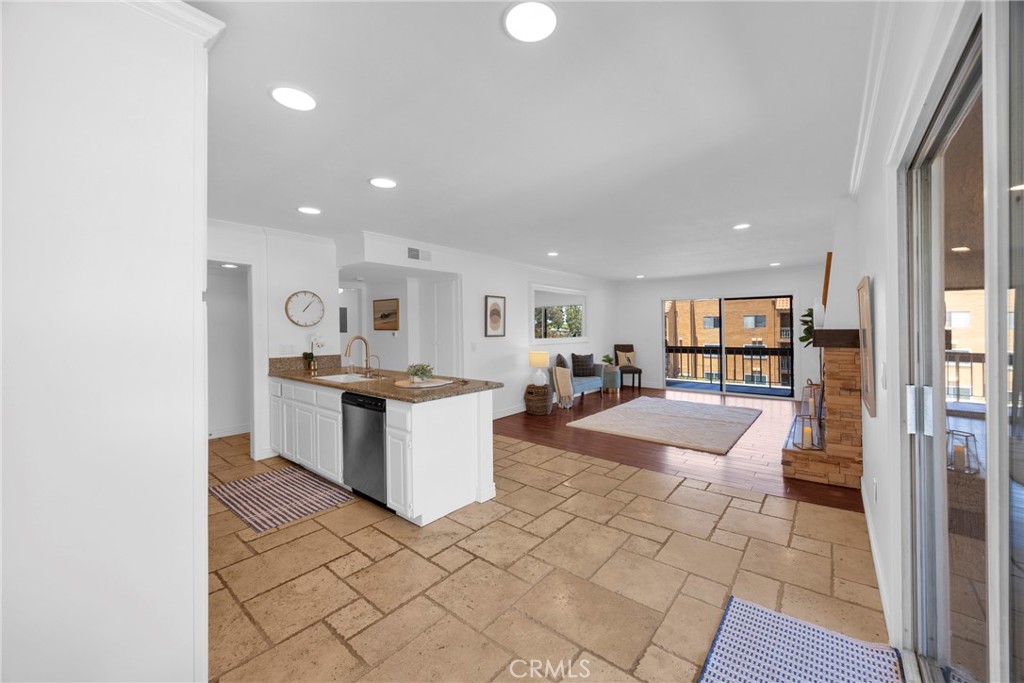 Open-plan kitchen and living area with a granite breakfast bar, stone tile floors, and a brick fireplace.