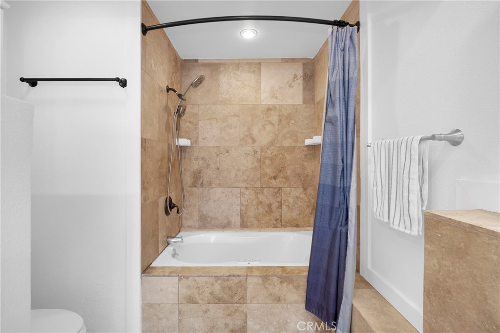 Bathroom with a tan stone-tiled tub and shower, blue curtain, and towel.