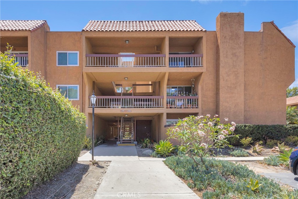 Condominium building with tan stucco, stacked balconies, and a landscaped walkway to the entrance.