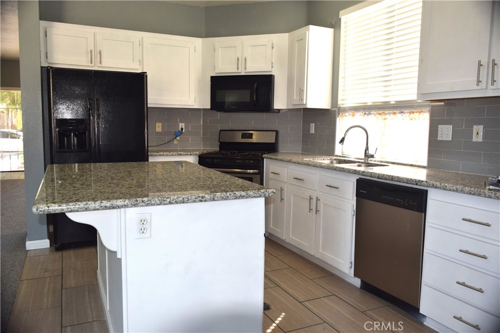 Kitchen with a large granite island, white cabinets, gray tile backsplash, and black appliances.