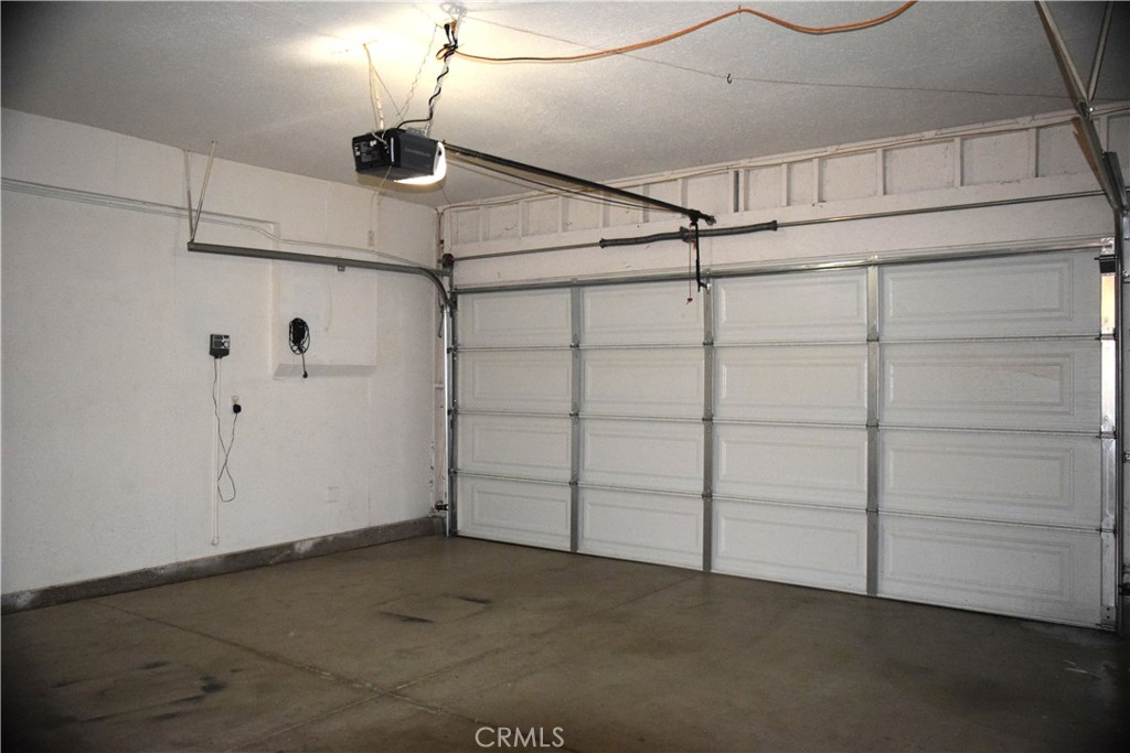 Empty garage with a closed sectional door, ceiling-mounted opener, and concrete floor.