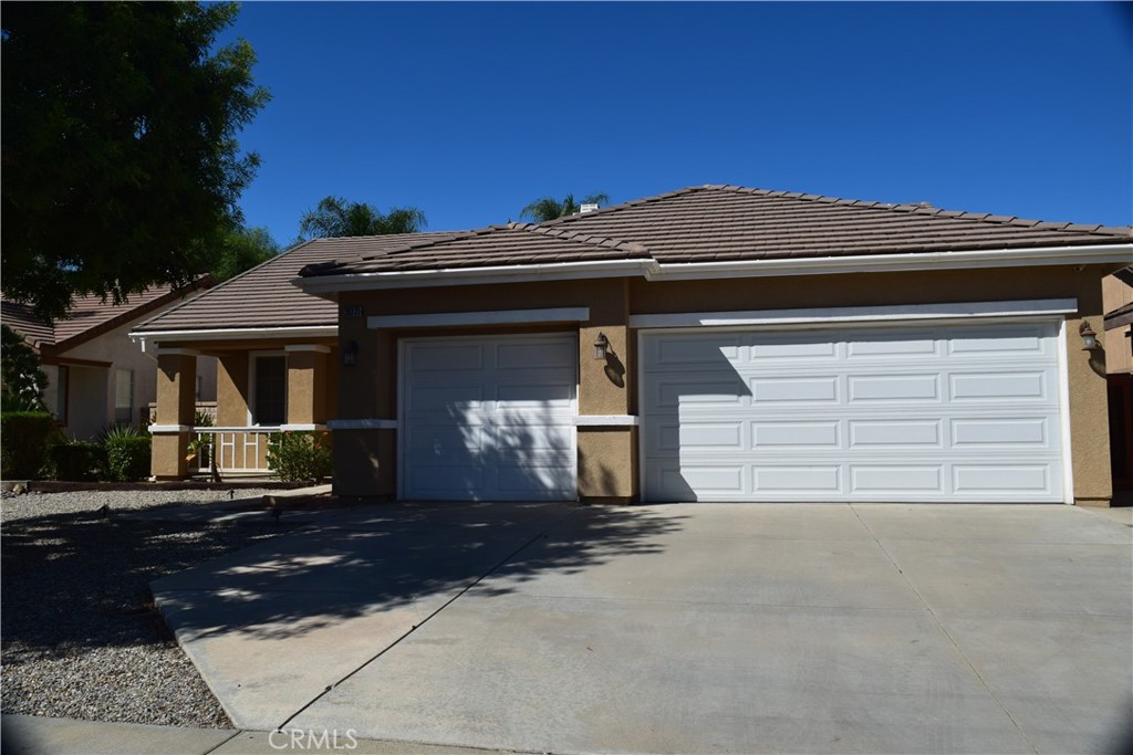 Tan stucco home with a tiled roof, two garage doors, and a broad concrete driveway.