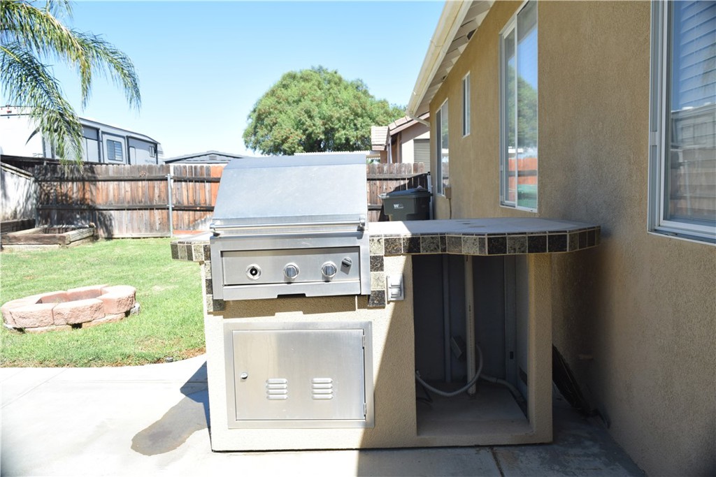 Backyard outdoor kitchen with a stainless steel grill and tiled island beside a lawn and stone fire pit.