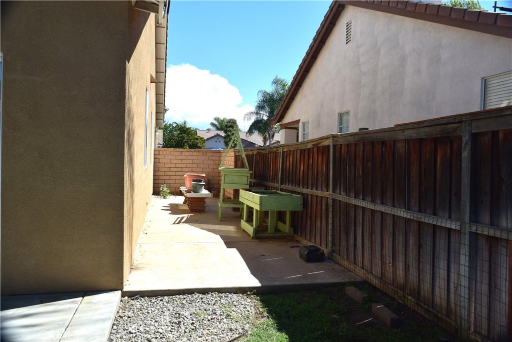 Side yard with a wooden fence, green raised planters, and a paved patio.